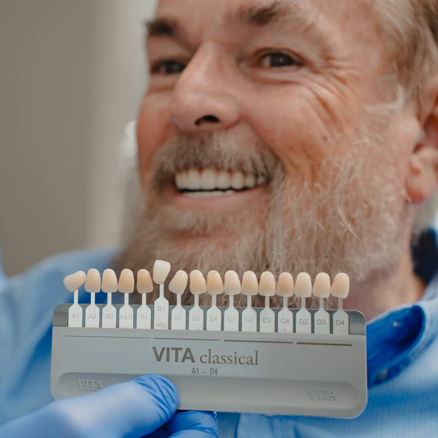 Sedation dentist matching tooth shade using dental shade guide beside smiling patient