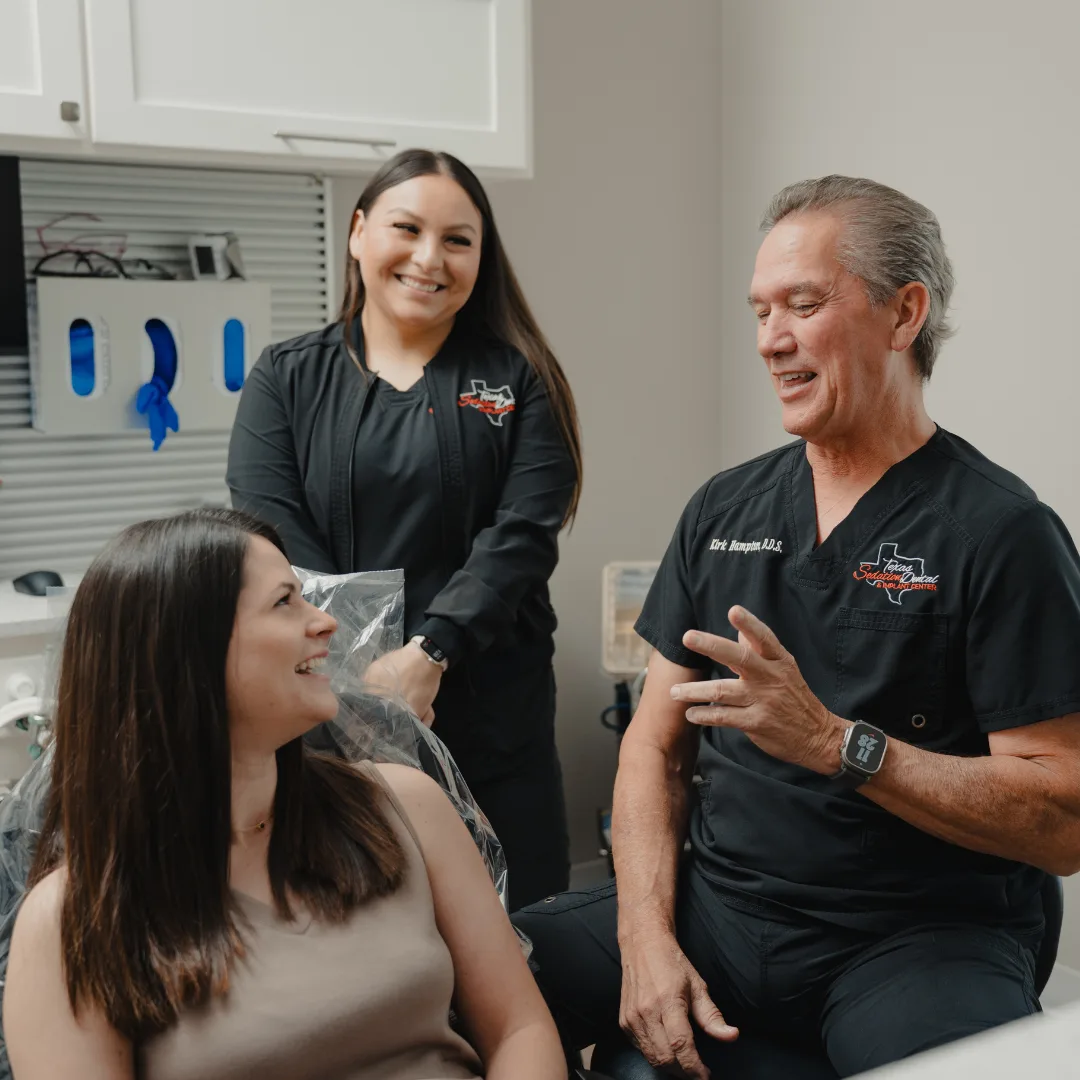 Sedation dentist consulting with patient while dental assistant smiles in treatment room