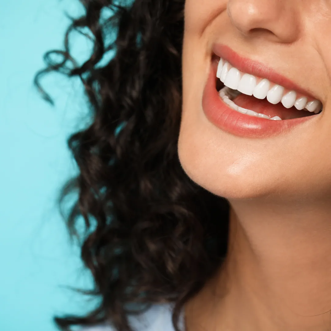 Close-up of smiling woman showing straight white teeth against blue background